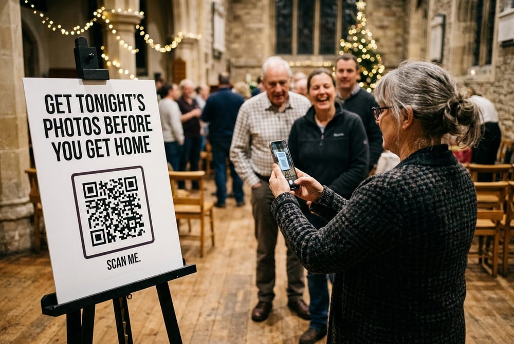 A sign at the head of a queue in a church hall, headed Get tonight&rsquo;s photos before you get home, above a large QR code. A woman holds up her phone to scan it while others wait behind her.